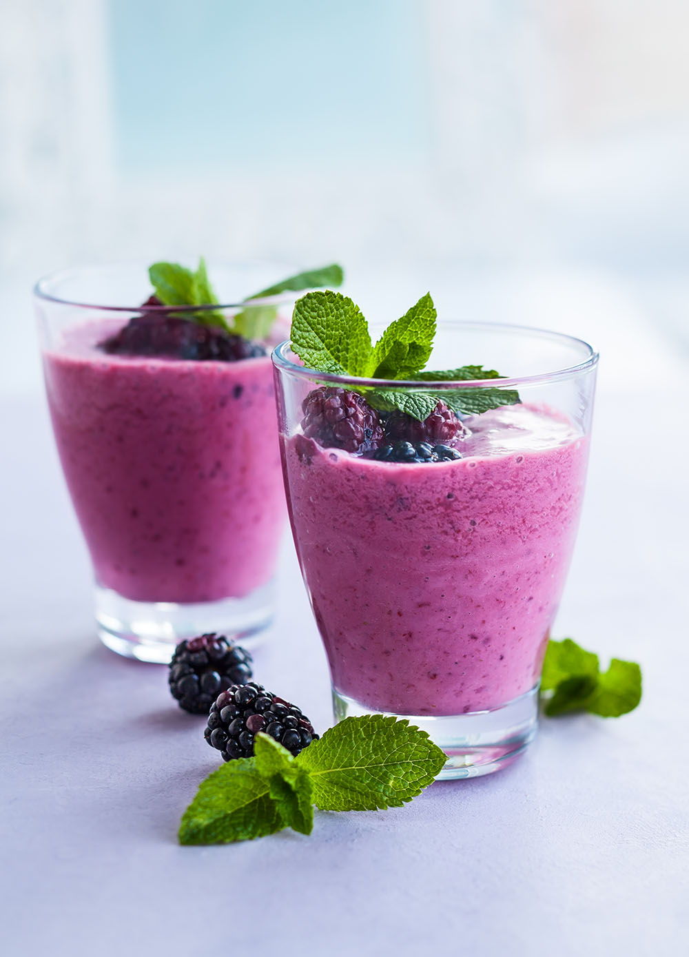 Zwei Gläser gefüllt mit dunkelrosa Brombeermousse, garniert mit Brombeeren und Melisse.